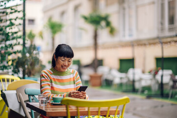 Happy japanese woman sitting in a garden cafe and enjoying her morning coffee.