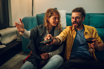 Boy turning up the volume on the TV while the girl is telling him to turn it do.