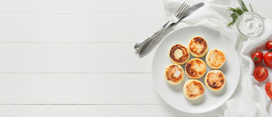 Plate with tasty cottage cheese pancakes and sauce on white wooden background with space for text
