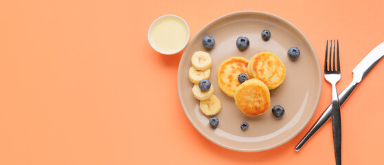 Plate with tasty cottage cheese pancakes, blueberry, banana and condensed milk on orange background...
