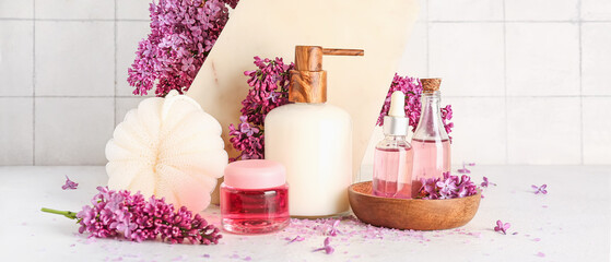 Bottle of liquid soap with serum, cosmetic gel, bast wisp and lilac flowers on light background