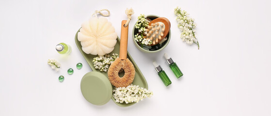 Bottles of serum with massage brush, bast wisp and lilac flowers on light background