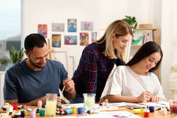 Fototapeta premium Artist teaching her students to paint at table in studio. Creative hobby