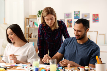 Fototapeta premium Artist teaching her students to paint at table in studio. Creative hobby