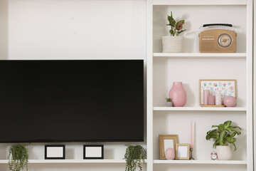 TV set and stylish shelves with decorative elements and houseplants near white wall. Interior design