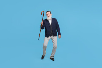 Fototapeta premium Cheerful senior man with walking cane on light blue background