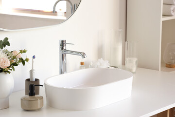 Fototapeta premium White sink with bath accessories and flowers on table in light bathroom, closeup