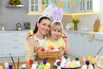 Naklejka premium Mother and her cute son with Easter eggs at table in kitchen