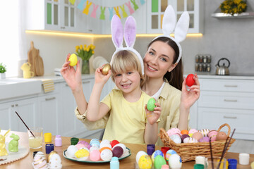 Mother and her cute son with Easter eggs at table in kitchen