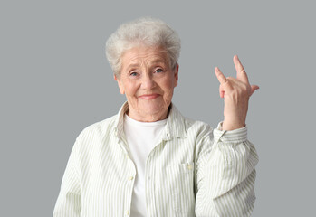Senior woman showing "i love you" gesture on grey background