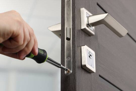 Handyman with screwdriver repairing door lock indoors, closeup