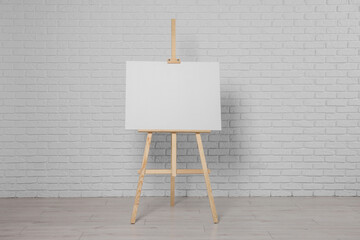 Wooden easel with blank canvas near white brick wall indoors - obrazy, fototapety, plakaty