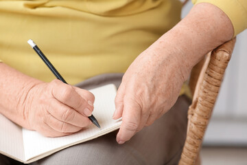 Senior woman writing in notebook at home, closeup