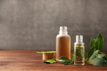 Obraz na płótnie Canvas Bottles of bay essential oil and fresh leaves on wooden table. Space for text