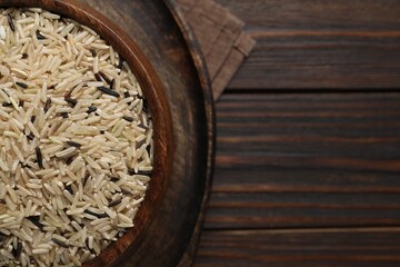 Bowl of raw unpolished rice on wooden table, top view. Space for text