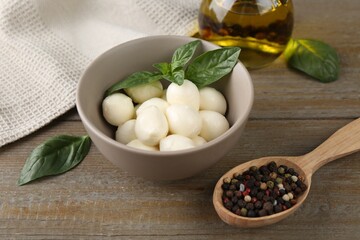 Tasty mozarella balls, basil leaves, oil and spices on wooden table