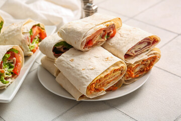 Plate of tasty lavash rolls with vegetables on white tile background