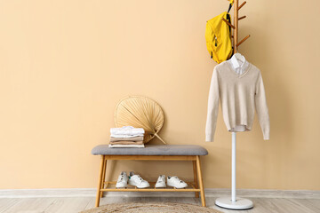 Stylish school cardigan with shirt, backpack hanging on rack, bench and sneakers near beige wall in...