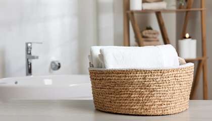 Wicker basket with white towels on table in bathroom. Space for text