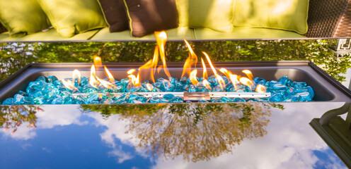 Glass Fire Table next to patio furniture and with a tree reflection on the glass