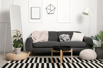 Interior of light living room with grey sofa, mirror and coffee table