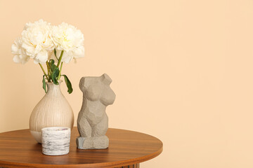Vase of white peonies and figurine on coffee table near beige wall