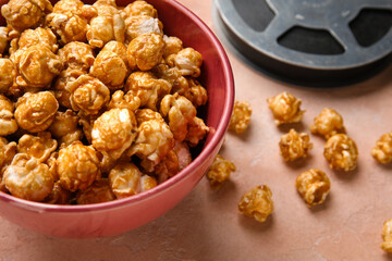 Bowl with tasty popcorn and film reel on pink background