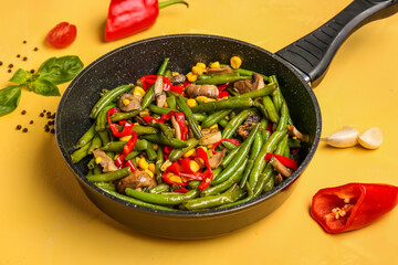Frying pan with different vegetables on yellow background