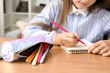 Little girl with pencil case drawing at table, closeup