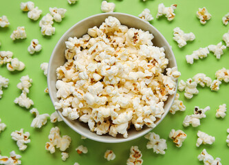 Bowl with tasty popcorn on green background