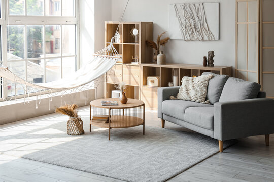 Interior of light living room with hammock, table and sofa
