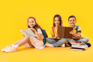 Little schoolchildren reading books on yellow background