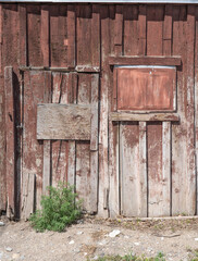 Old wooden door with wall is patched and sealed with boards. Slats of wood are weathered with lots of texture and old peeling paint in red or brown