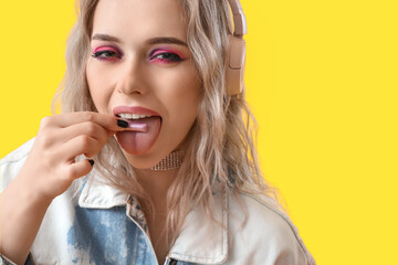 Young woman in headphones eating candy on yellow background, closeup