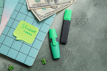 Green markers, notebook, dollar banknotes and sticky note with text STUDENT LOANS on grey background