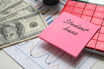 Sticky note with text STUDENT LOANS, calculator and dollar banknotes on table, closeup