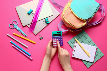 Woman with different stationery and backpack using calculator on pink background