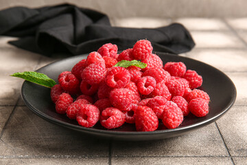 Plate with fresh raspberries and mint on grey tile table