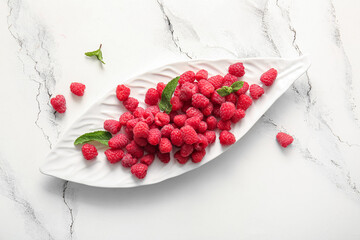 Plate with fresh raspberries and mint on white background