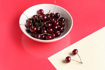 Bowl with sweet cherries on colorful background