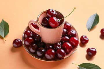 Cup and plate with sweet cherries on orange background