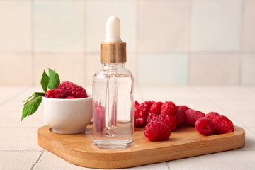 Wooden board with bottle of cosmetic raspberry oil on white tile background