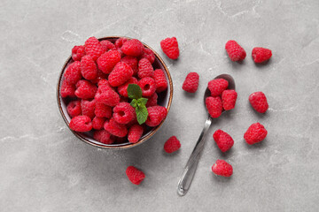 Bowl with fresh raspberry and spoon on grey background