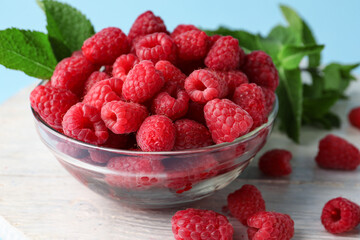 Glass bowl with fresh raspberries and mint on blue background, closeup