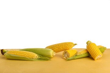 Fresh corn cobs on yellow table against white background