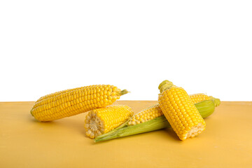 Fresh corn cobs on yellow table against white background