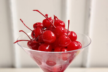 Glass of tasty maraschino cherries on white wooden background