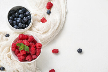 Bowls with fresh raspberry and blueberry on light background