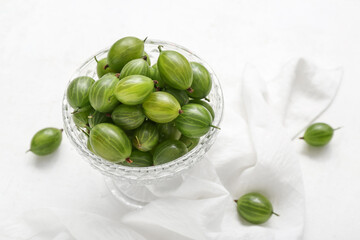 Glass bowl with fresh green gooseberry on white background, closeup