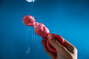 Woman pouring lubricant on pink anal beads on blue background. 